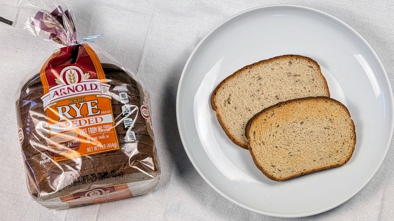 A loaf of Arnold Jewish rye bread next to a white plate with two slices of bread on a white tablecloth
