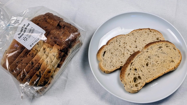A loaf of Freshness Guaranteed seeded sandwich rye next to a white plate with two slices of bread on a white tableclothnext to a white plate with two slices of bread on a white tablecloth