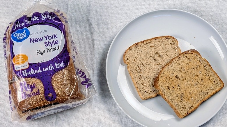 A loaf of Great Value New York-style rye next to a white plate with two slices of bread on a white tableclothnext to a white plate with two slices of bread on a white tablecloth
