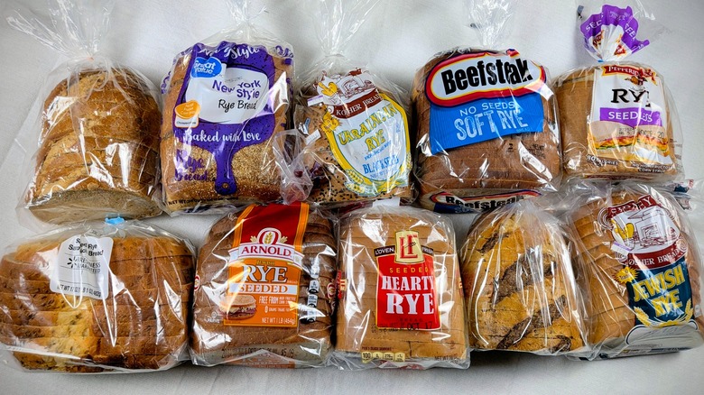 A top view of 10 loaves of different rye breads lined up in two rows on a white tablecloth