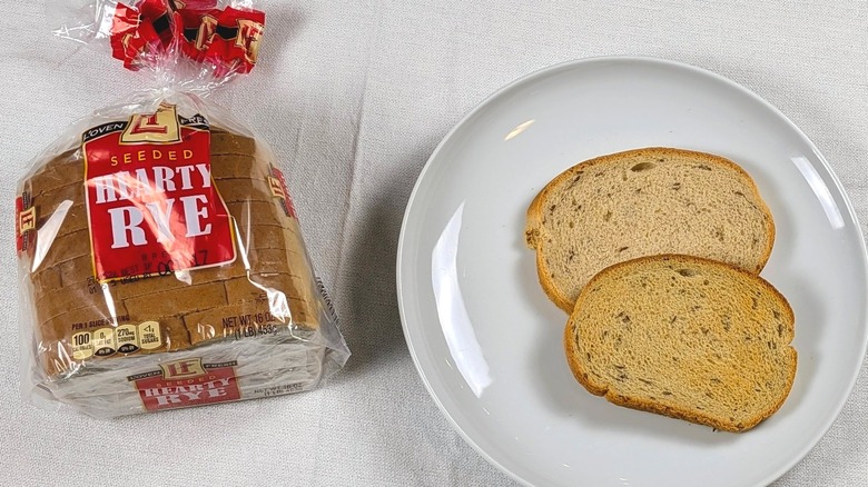 A loaf of L'Oven Hearty Rye next to a white plate with two slices of bread on a white tablecloth