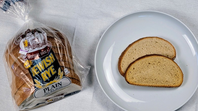 A loaf of Sidney's Jewish rye next to a white plate with two slices of bread on a white tableclothnext to a white plate with two slices of bread on a white tablecloth