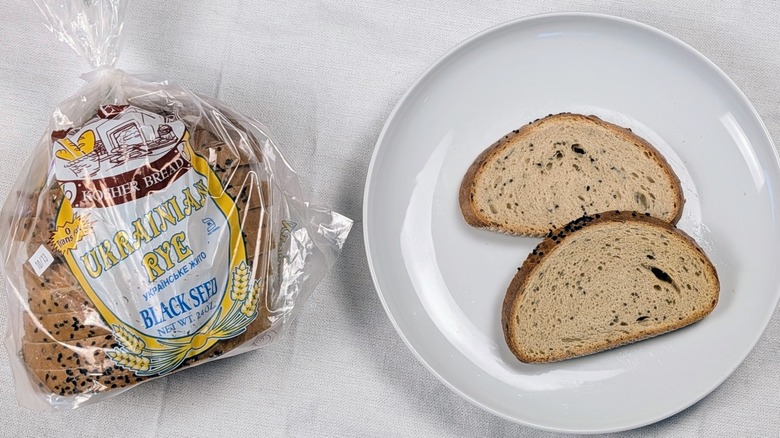 A loaf of Sidney's Ukrainian rye  next to a white plate with two slices of bread on a white tableclothnext to a white plate with two slices of bread on a white tablecloth