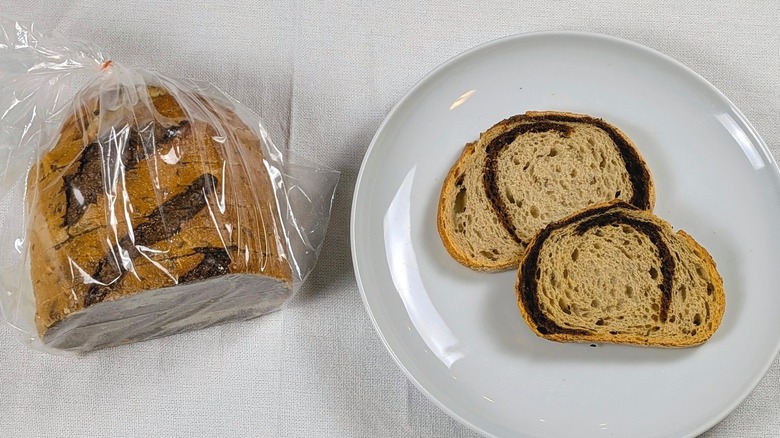A loaf of Wegmans marbled rye next to a white plate with two slices of bread on a white tableclothnext to a white plate with two slices of bread on a white tablecloth