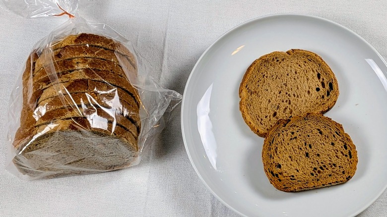 A loaf of Wegman's soft rye next to a white plate with two slices of bread on a white tableclothnext to a white plate with two slices of bread on a white tablecloth