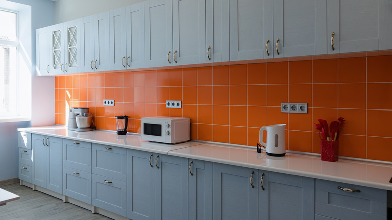 A well-organized kitchen featuring blue cabinets, orange tiles, and modern appliances creates an inviting space for cooking and socializing