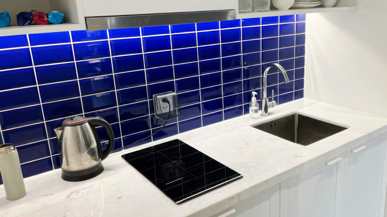 A kitchen counter with a skink and a square blue tile backsplash