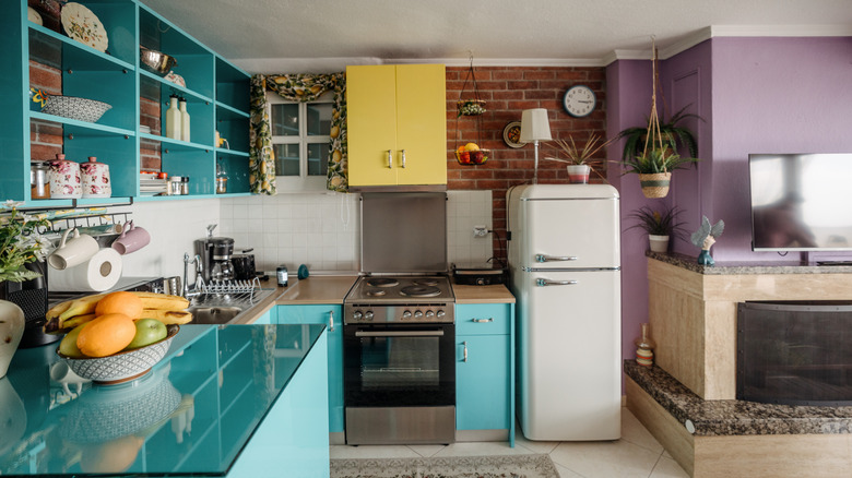 A kitchen with teal and yellow cabinets and a purple accent wall