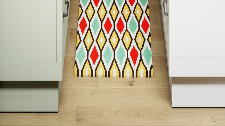 Multi-colored rug placed between white kitchen cabinets