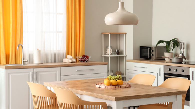 Interior of modern kitchen with white counters, dining table, yellow curtains, chairs and lamp