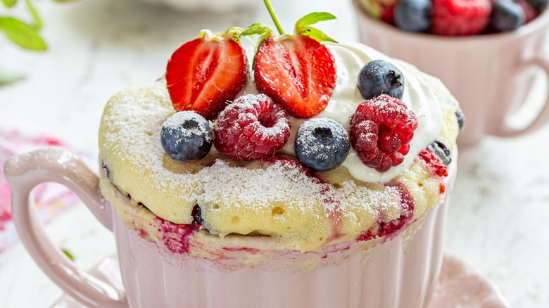 summery mug cake with berries cooked into a white-cake batter, garnished with fresh berries, served in pink mugs wiht matching saucers