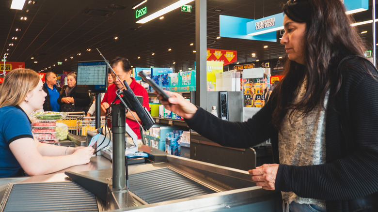 A woman pays for groceries at a checkout counter in a busy Aldi