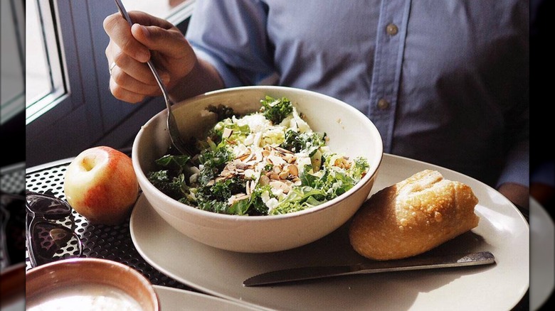 Unidentified customer eating bowl of salad on plate with bread and apple from Panera
