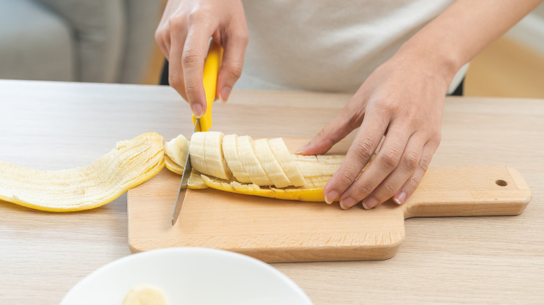 Person slicing banana on wooden cutting board
