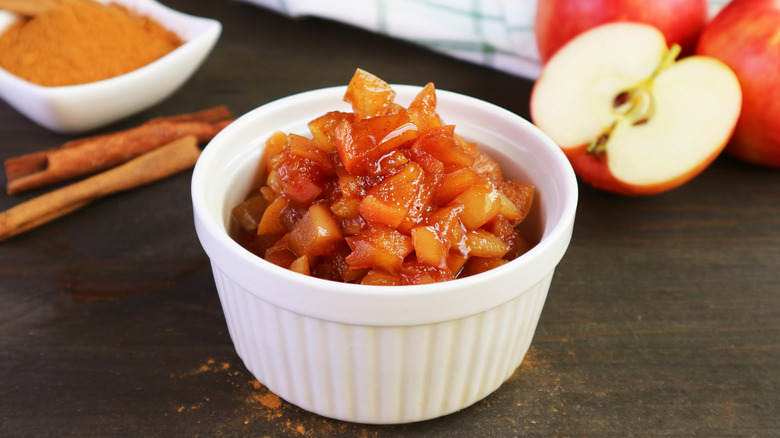 Caramelized apples in white bowl next to cinnamon and fresh apples