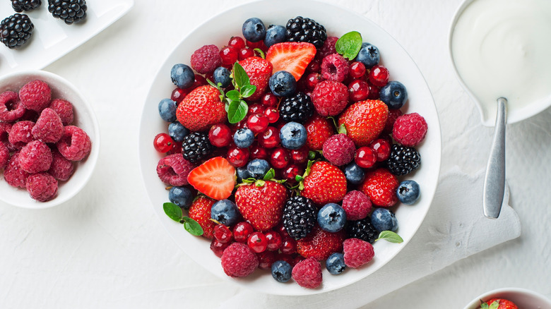 Bowl of fresh berries next to bowl of yogurt with spoon