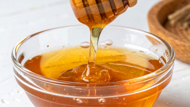 Honey drizzling from wooden dipper into bowl