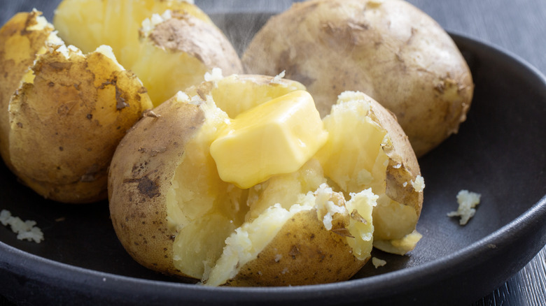 Steaming baked potatoes with butter on plate