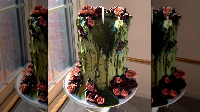 ornate green cake with roses scattered throughout and a single candle in the middle