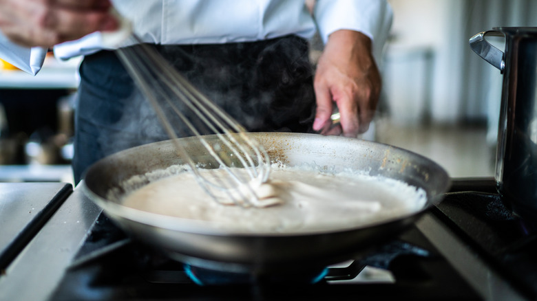 Cook whisking white cream sauce in pan on stove top.