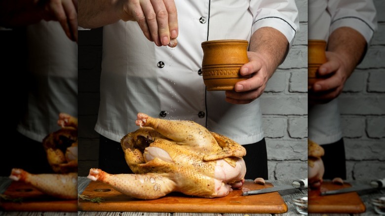 Chef sprinkling seasoning on whole chicken