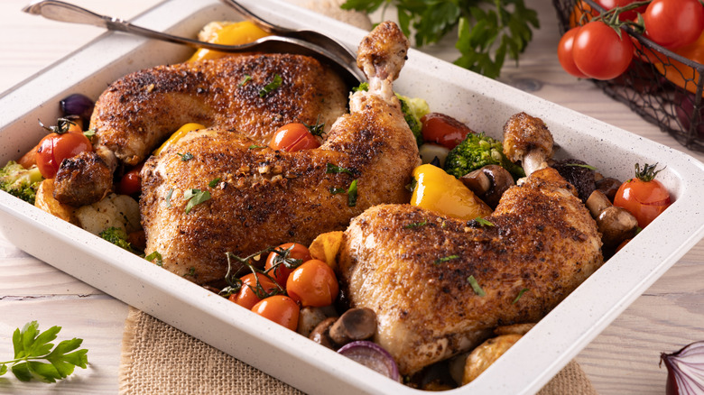 White baking dish with roasted seasoned chicken pieces and vegetables.