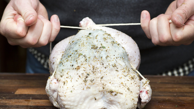 Close up of hands trussing a chicken on wood surface.