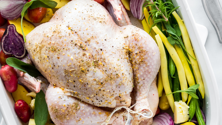 Whole raw chicken with seasonings and vegetables in shallow white dish