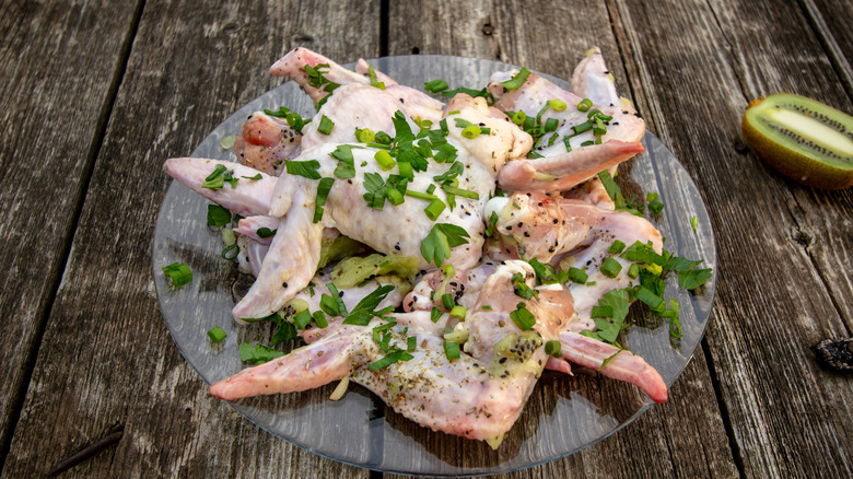 Raw pieces of chicken on round glass platter with chopped parsley, dill, and chives on top.