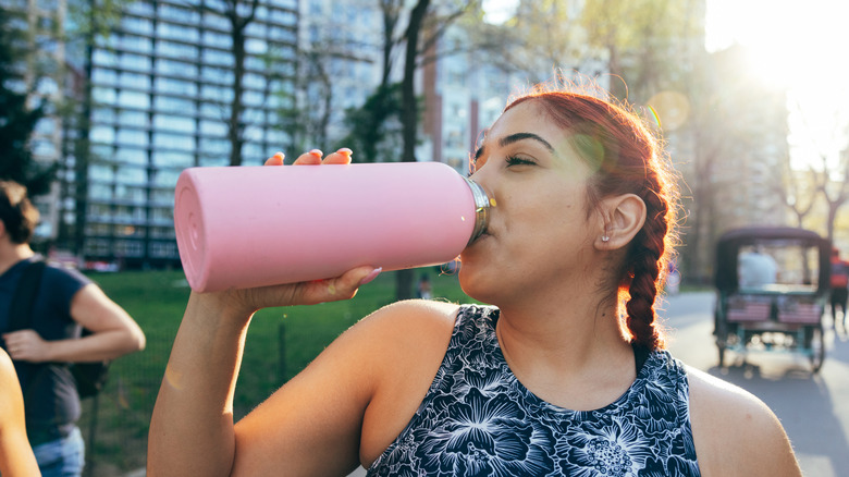 A woman drinking from a pink water bottle after a run