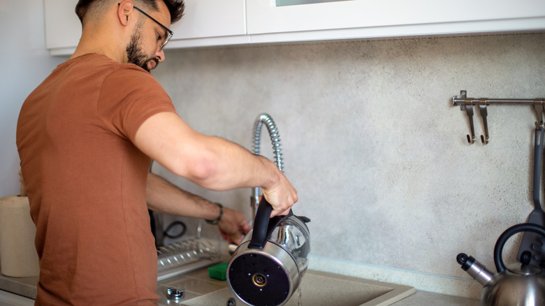 Man pouring water from an electric kettle into the sink