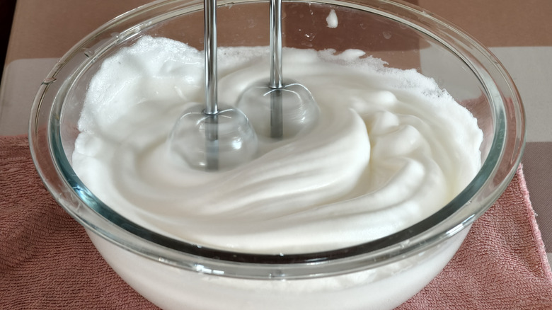 Cream being whipped in a glass bowl with a hand mixer