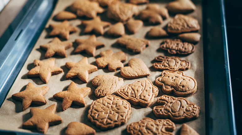 Overhead view of gingerbread cookies in baking sheet by pastry cutters on table