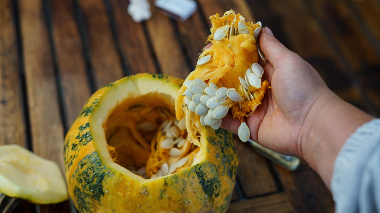 Hand removing pumpkin pulp and seeds from pumpkin