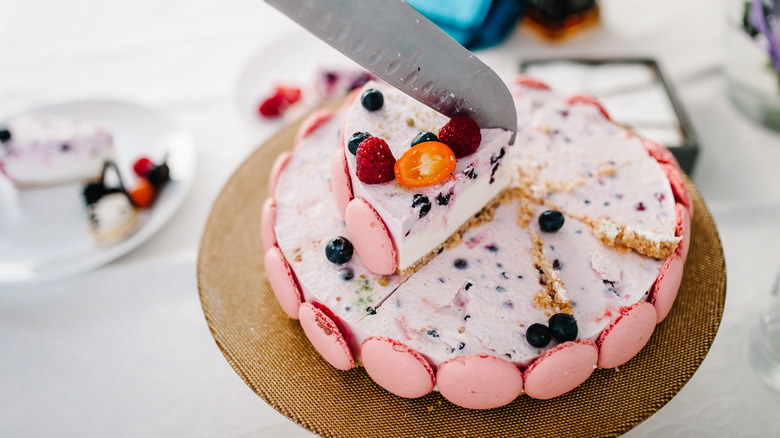 Top view of a knife slicing a pink cake decorated with macarons
