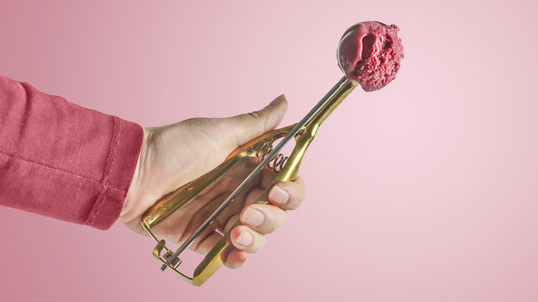 Hand holding a scoop of pink fruity ice cream against a pink background