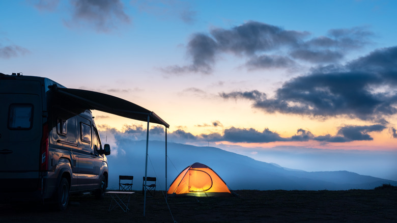 A van and a brightly-lit tent on a campsite near mountains at dusk