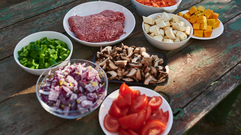 Various pre-chopped ingredients in white bowls on a picnic table outside
