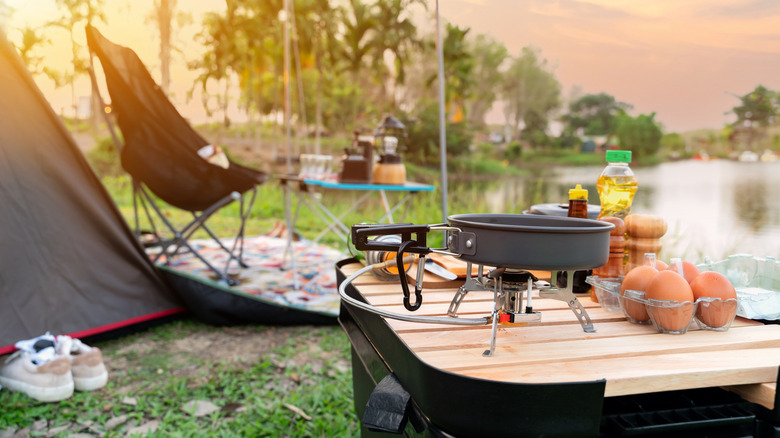 Eggs, oil, and cooking gear on a small table in front of a tent and lake