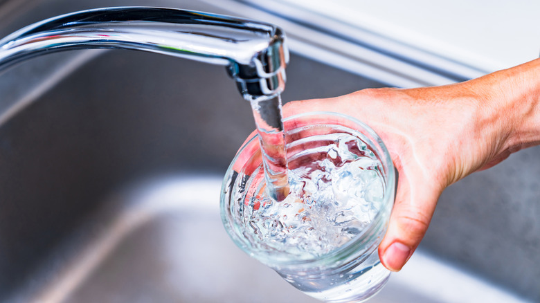 Hand holding cup that's being filled with water from faucet