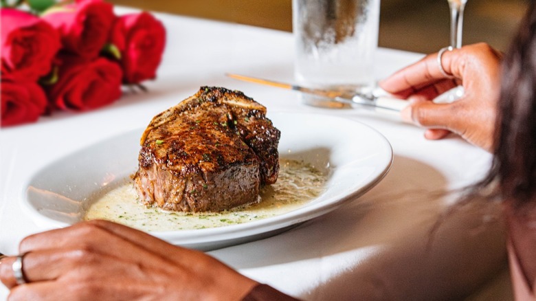 Steak on white plate at Ruth's Chris with hands ready to eat