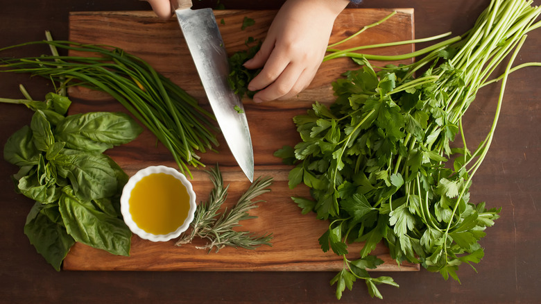 Top view of someone cutting fresh herbs on a wooden cutting board