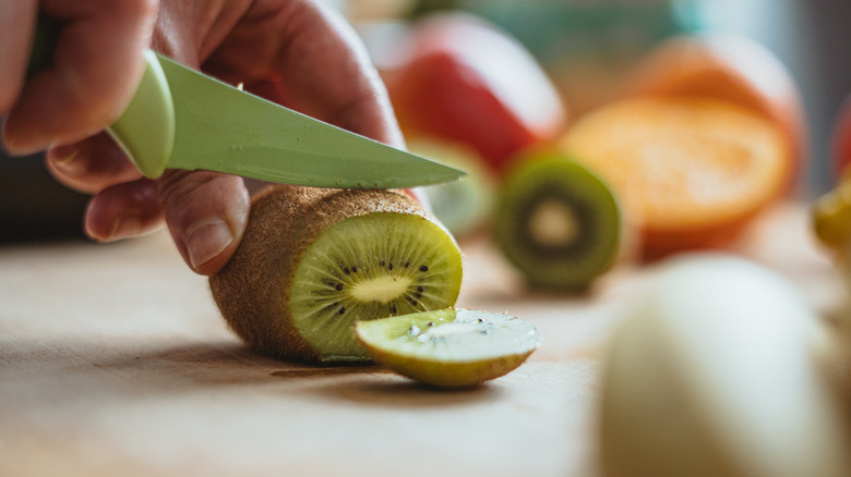Hand and knife slicing kiwi on cutting board