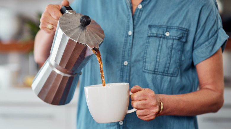 Woman pouring coffee from Moka pot into white coffee cup
