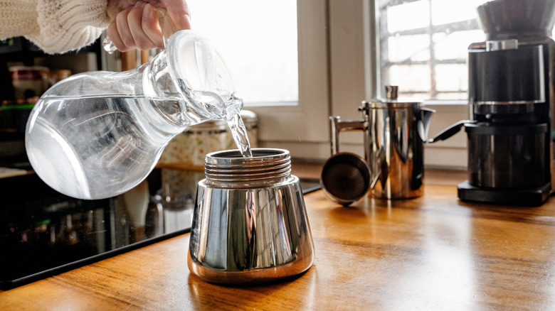 Hand pouring water from pitcher into bottom reservoir of Moka pot