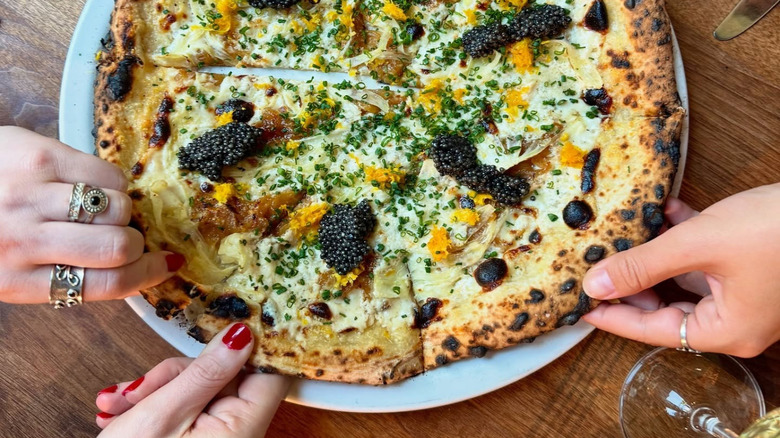 Hands grabbing slices of caviar pizza