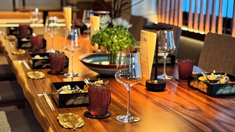 Wooden table elegantly set with empty wine glasses, chopsticks, and folded menus