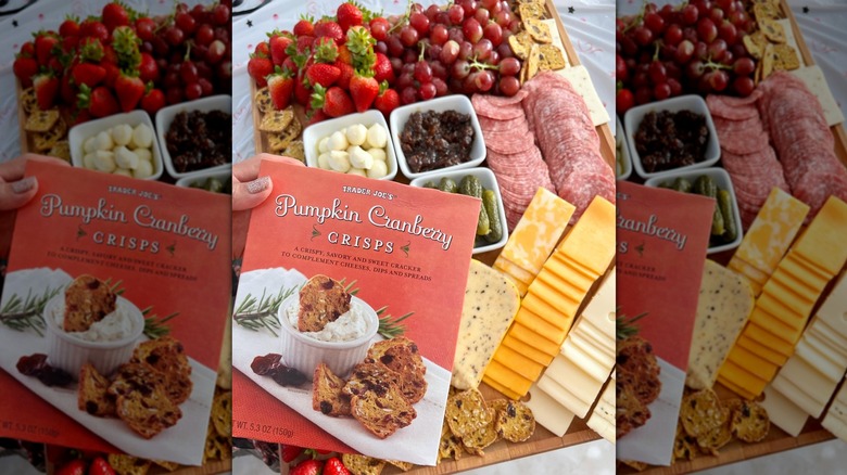 Hand holding box of Trader Joe's Pumpkin Cranberry Crisps in front of charcuterie board