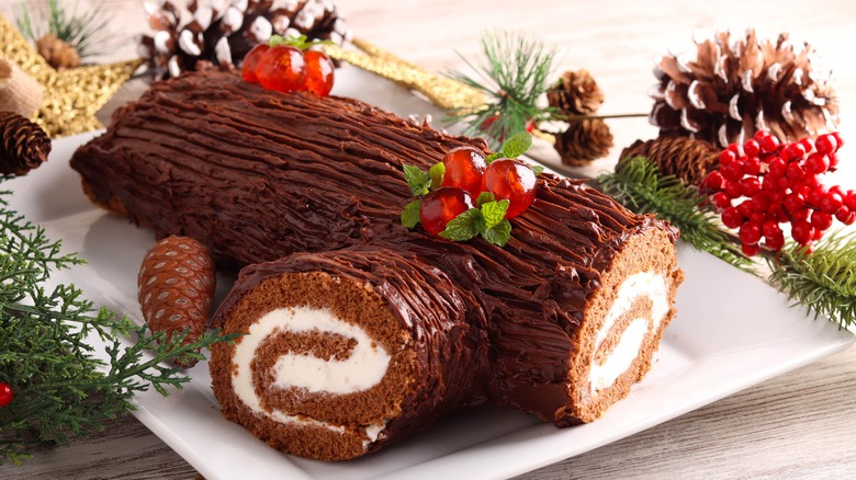 a festive Bûche de Noël cake surrounded by pinecones and berries