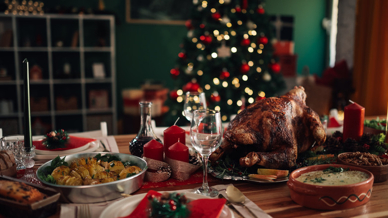 set dining table with roast turkey and sides in front of a lit Christmas tree
